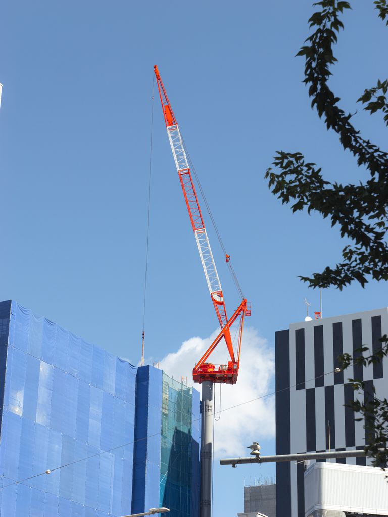 A view of a construction site featuring a prominent red and white tower crane against a clear blue sky in Nagoya, Japan.